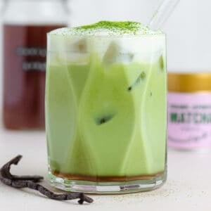 A matcha latte with cold foam on top dusted with matcha for garnish and a glass straw.