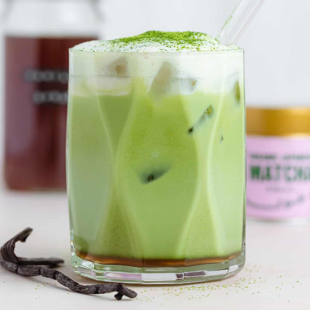 A matcha latte with cold foam on top dusted with matcha for garnish and a glass straw.