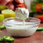 A hand dipping a cauliflower wing into creamy jalapeno mayo with visible tiny pieces of jalapenos.