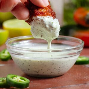 A hand dipping a cauliflower wing into creamy jalapeno mayo with visible tiny pieces of jalapenos.