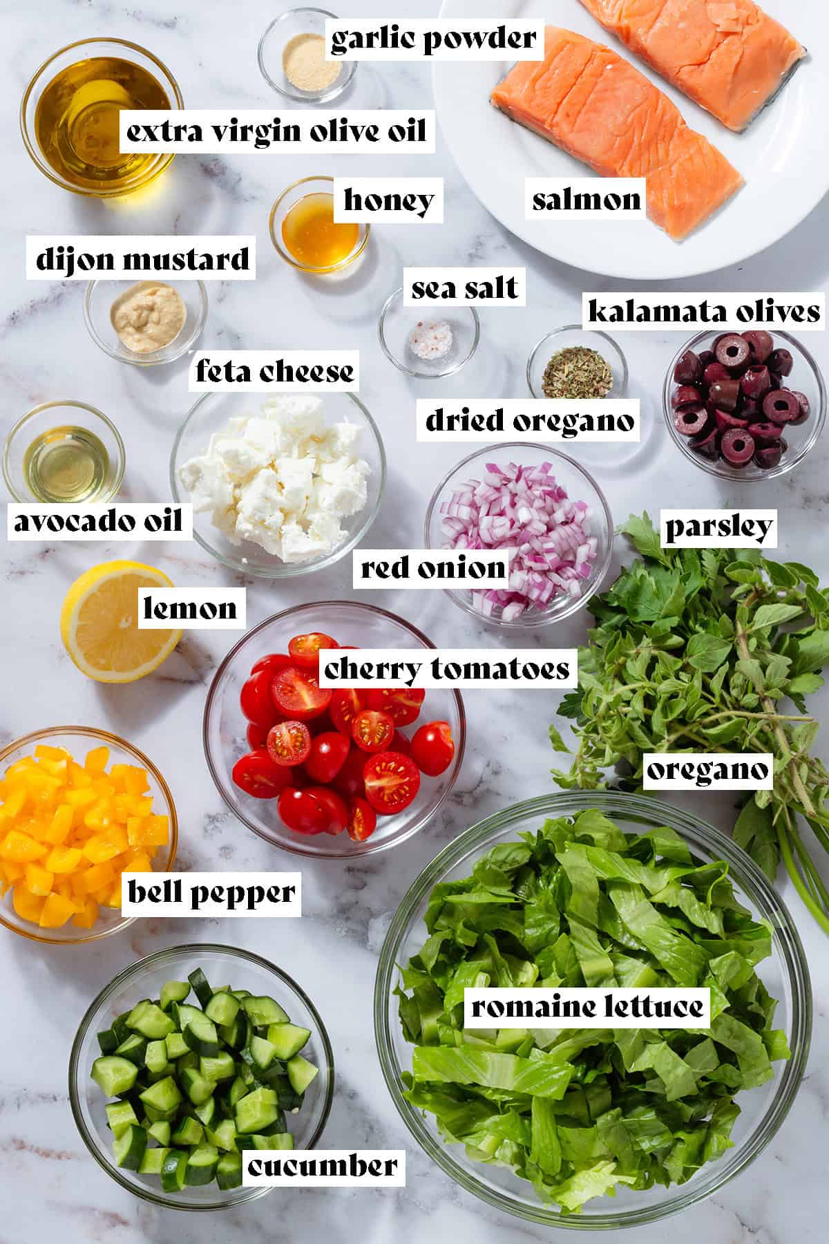 Chopped romaine lettuce, cucumber, cherry tomatoes, bell peppers, red onion, and other ingredients like raw salmon, feta, and olives in glass bowls.