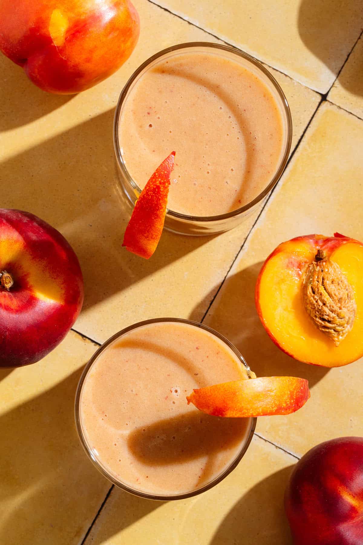 Bright orange nectarine smoothie in two glasses garnished with nectarine wedges.