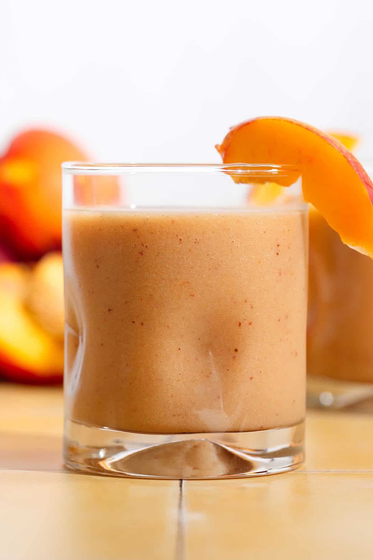 A short glass with bright orange nectarine smoothie garnished with a nectarine wedge.