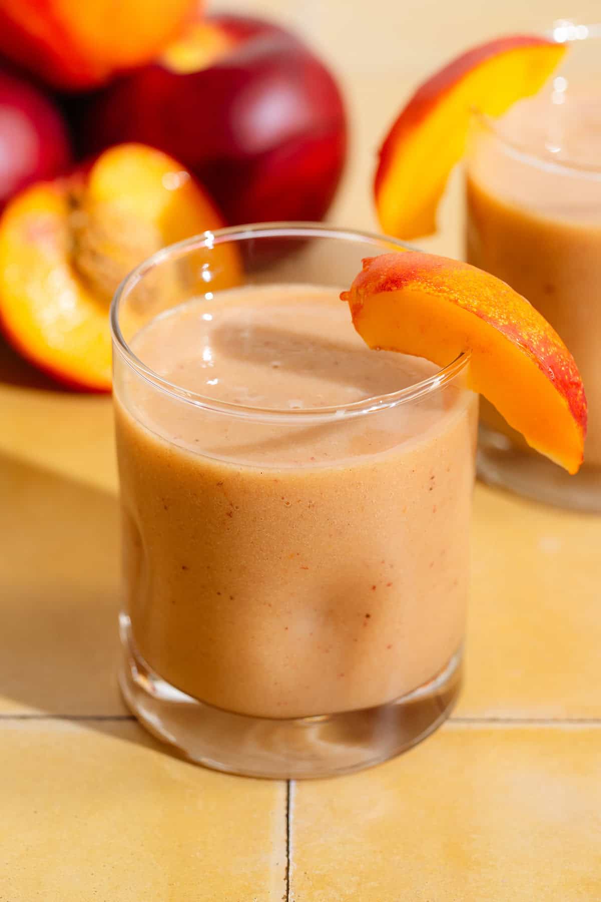 A short glass with bright orange nectarine smoothie garnished with a nectarine wedge.