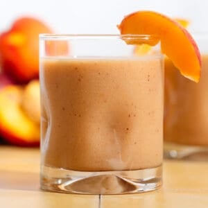 A short glass with bright orange nectarine smoothie garnished with a nectarine wedge.