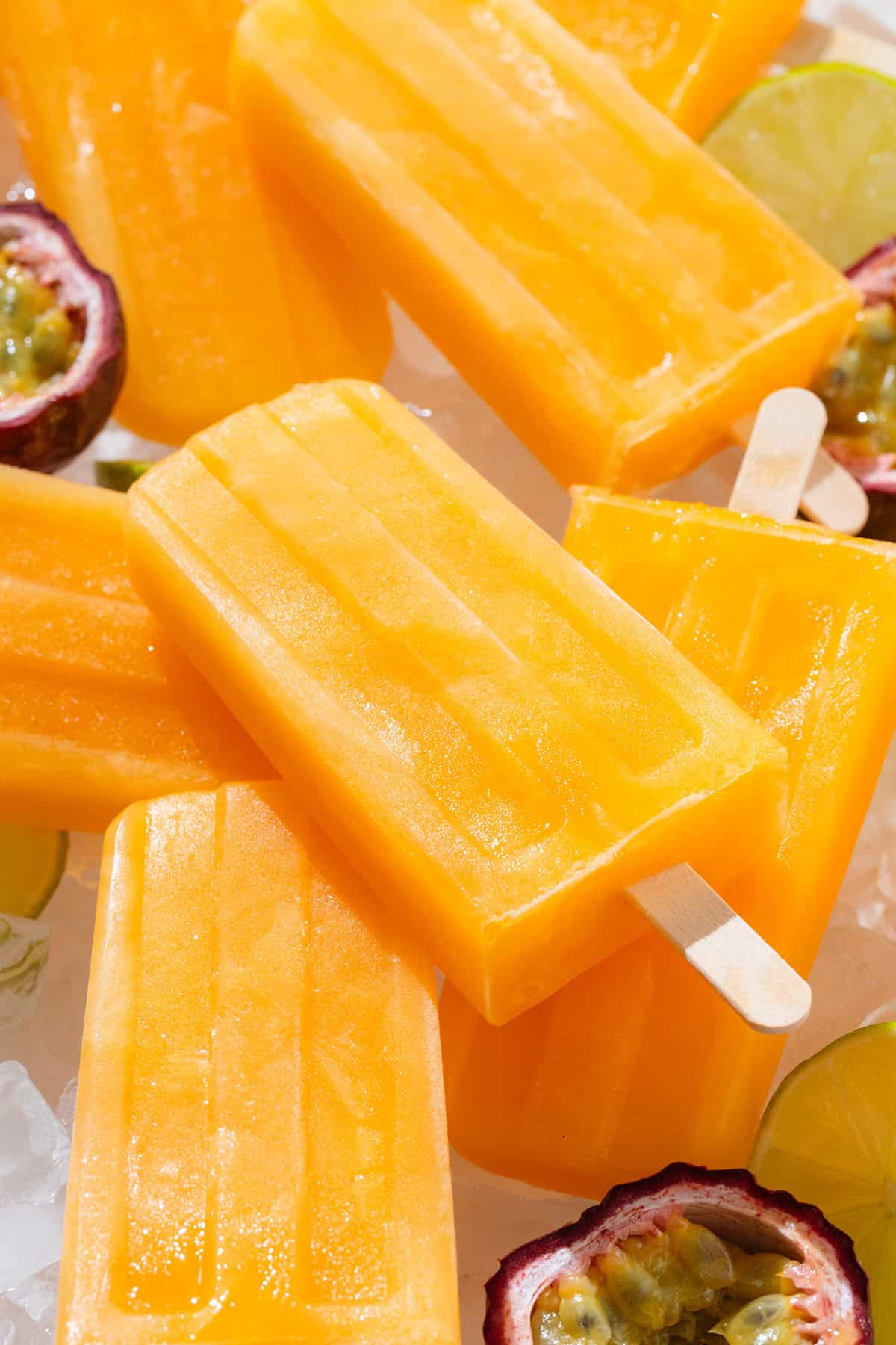 Bright orange popsicles on a white plate with ice and halves of fresh passion fruit.