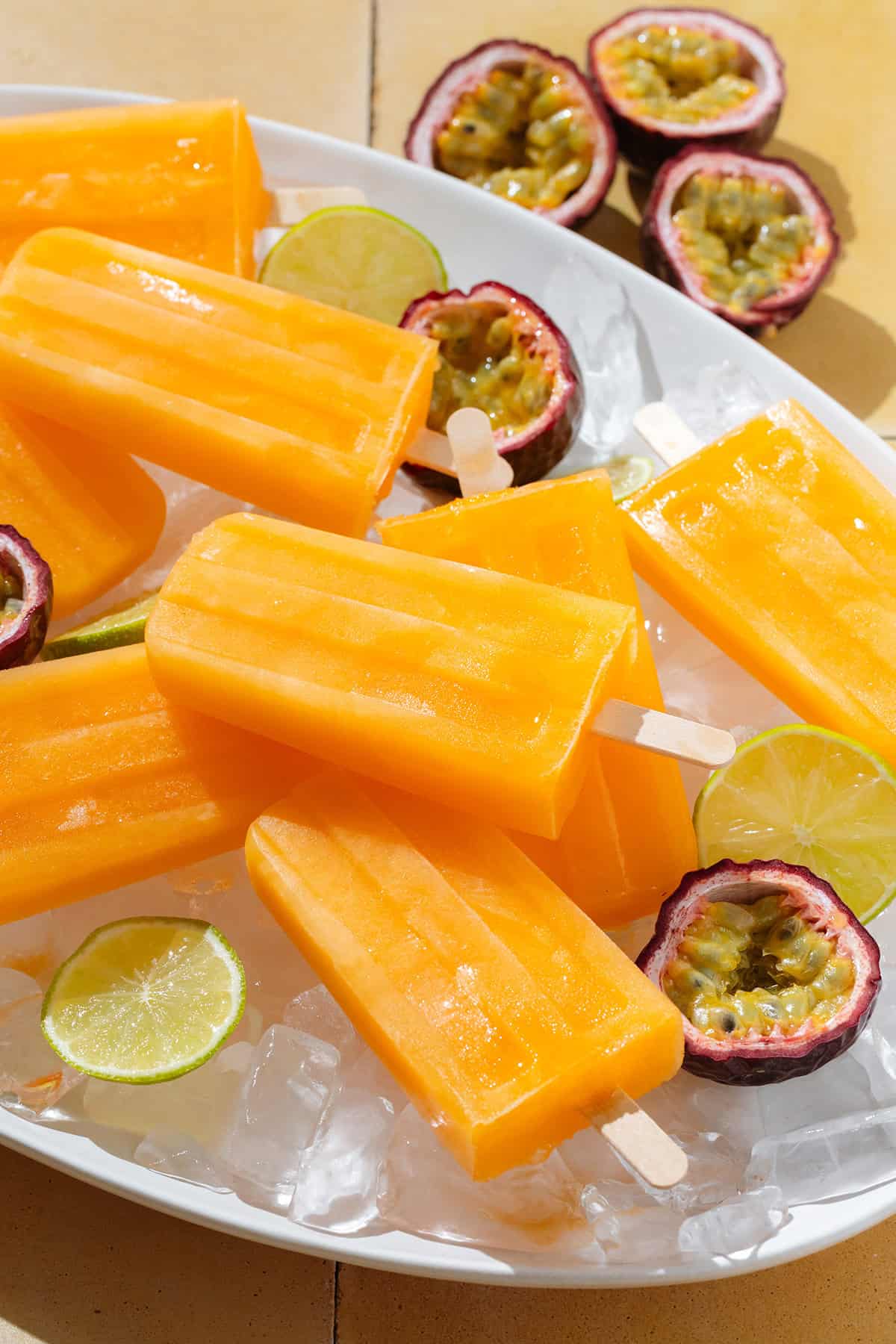 A plate of bright orange popsicles laying on ice with fresh passion fruit and lime slices.