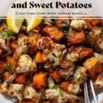Roasted caramelized diced sweet potato and cauliflower florets in a white bowl sprinkled with flaky sea salt and chopped fresh parsley and with two lemon wedges on the left and two forks on the right.