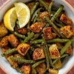 Crispy golden roasted diced potatoes and green beans in a white bowl with two lemon wedges on the left.