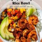 A bowl with cilantro rice, spicy shrimp, mango pico de gallo, slice avocado, and two lemon wedges.