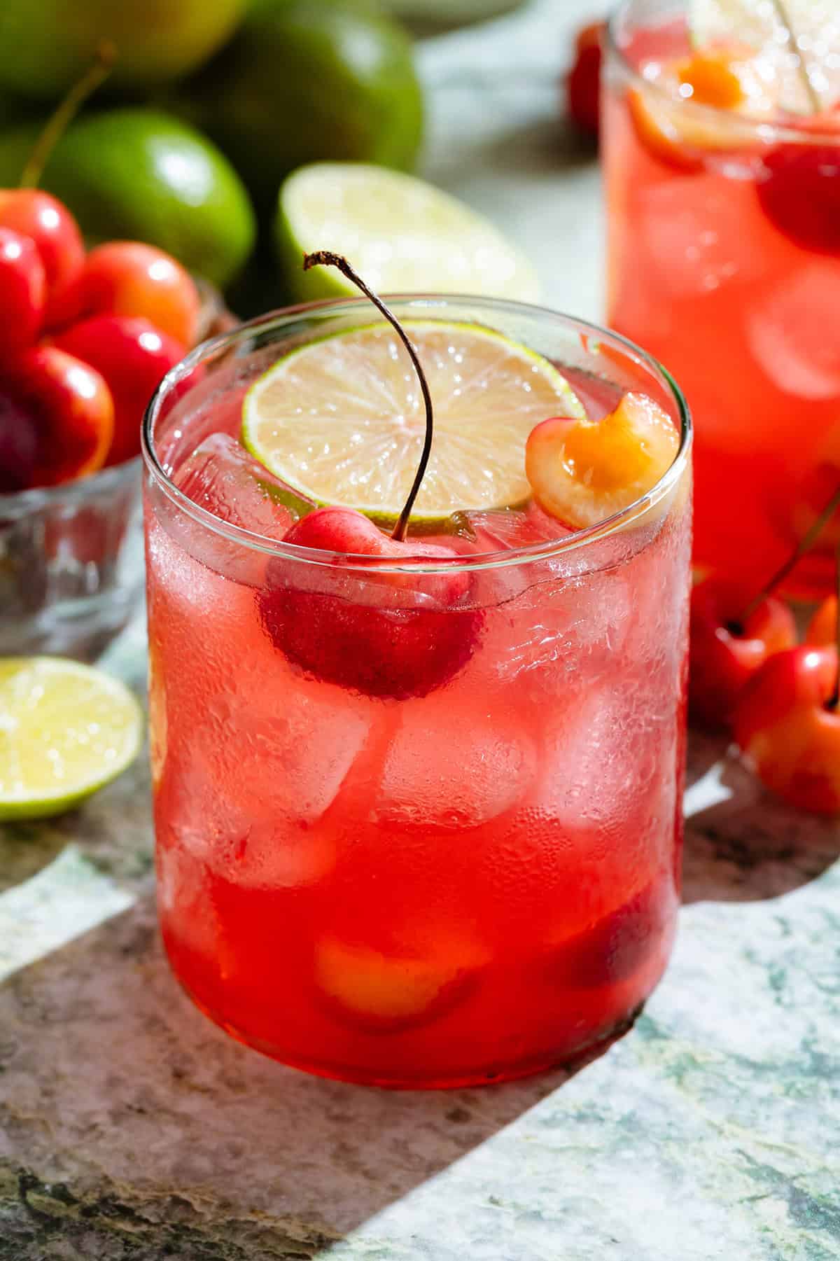 Bright red cherry margarita in a short glass garnished with a slice of lime and fresh cherries.