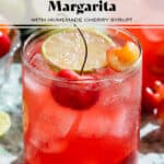 Bright red cherry margarita in a short glass garnished with a slice of lime and fresh cherries.