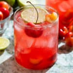 Bright red cherry margarita in a short glass garnished with a slice of lime and fresh cherries.