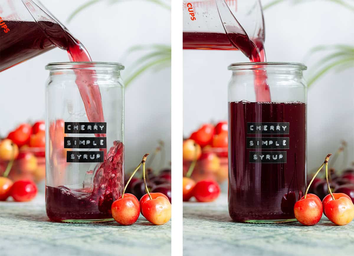 Dark red cherry syrup being poured into a tall glass jar with light and dark cherries all around it.
