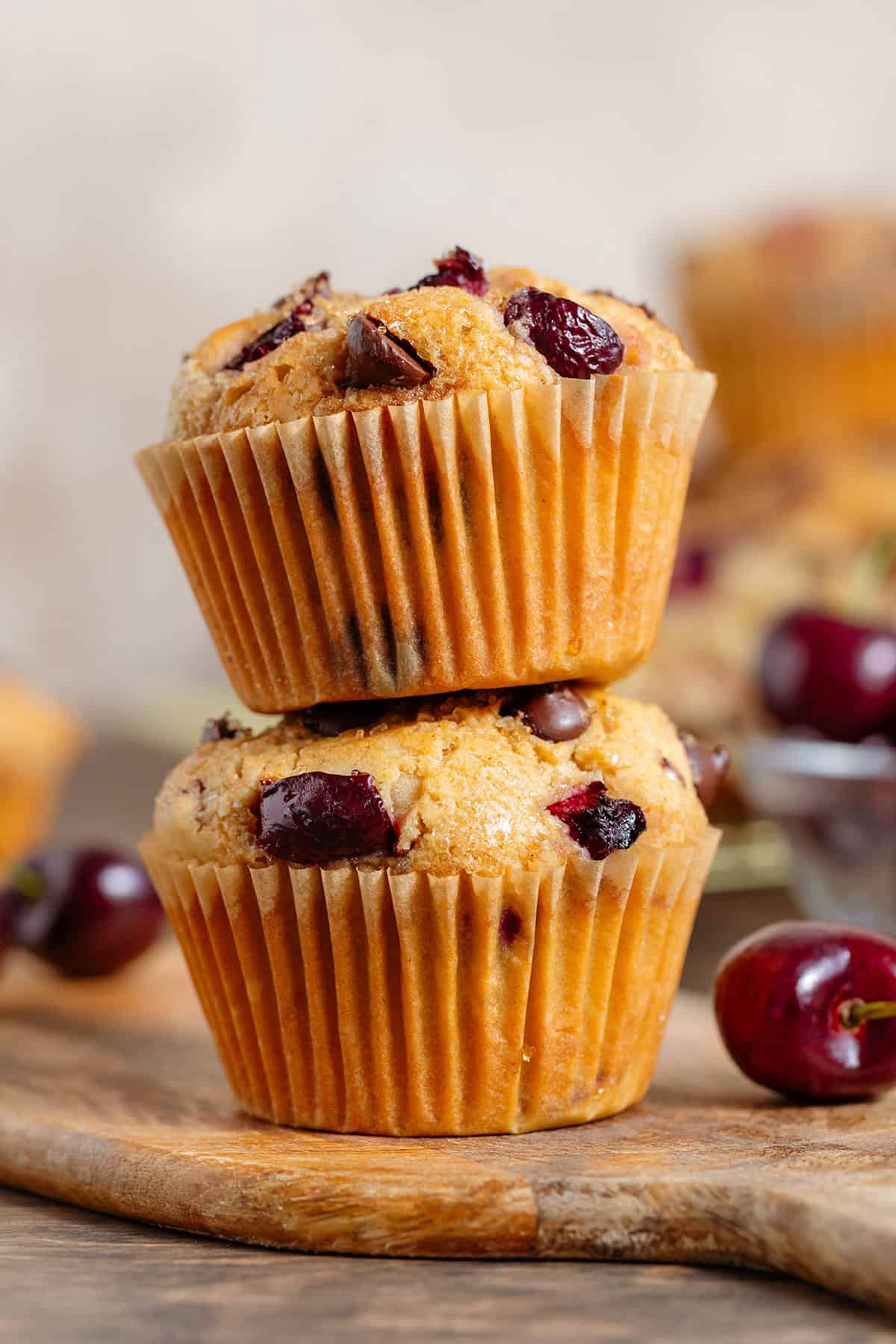 Two cherry and chocolate muffins stacked on a small wooden board.
