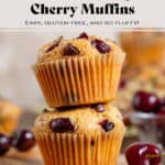 Two cherry and chocolate muffins stacked on a small wooden board with fresh cherries around them.