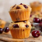Two cherry and chocolate muffins stacked on a small wooden board.