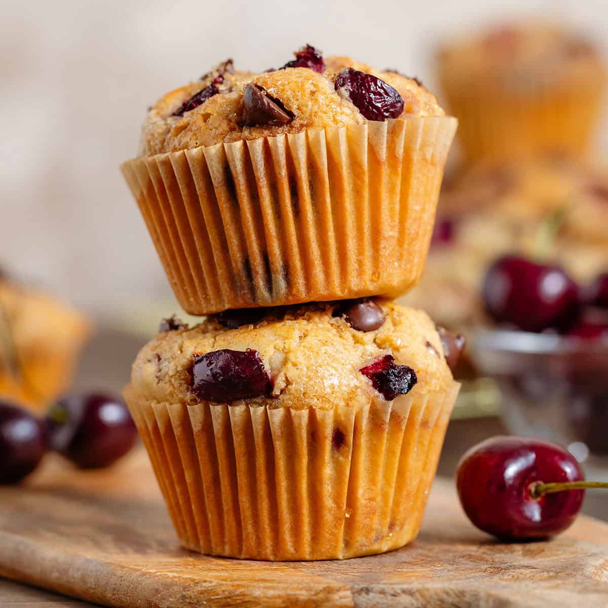 Two cherry and chocolate muffins stacked on a small wooden board.