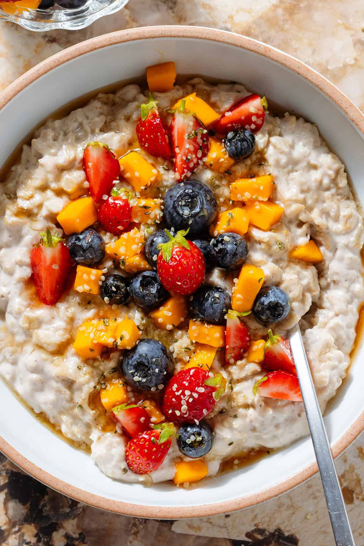 Creamy yogurt oatmeal in a white bowl with a beige rim topped with blueberries, strawberries, and chopped mango.