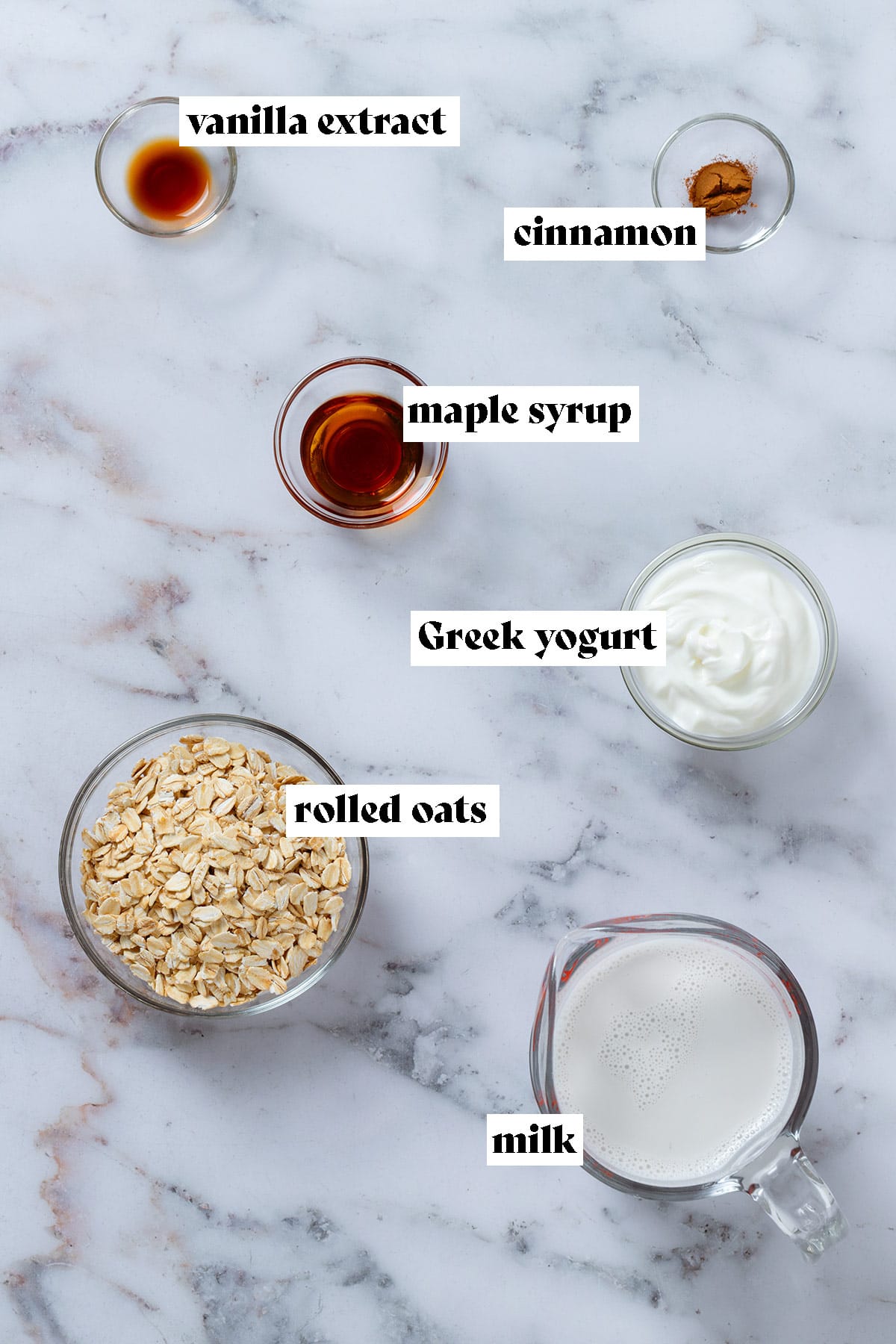 Oats, Greek yogurt, milk, maple syrup, and spices in small glass bowls.