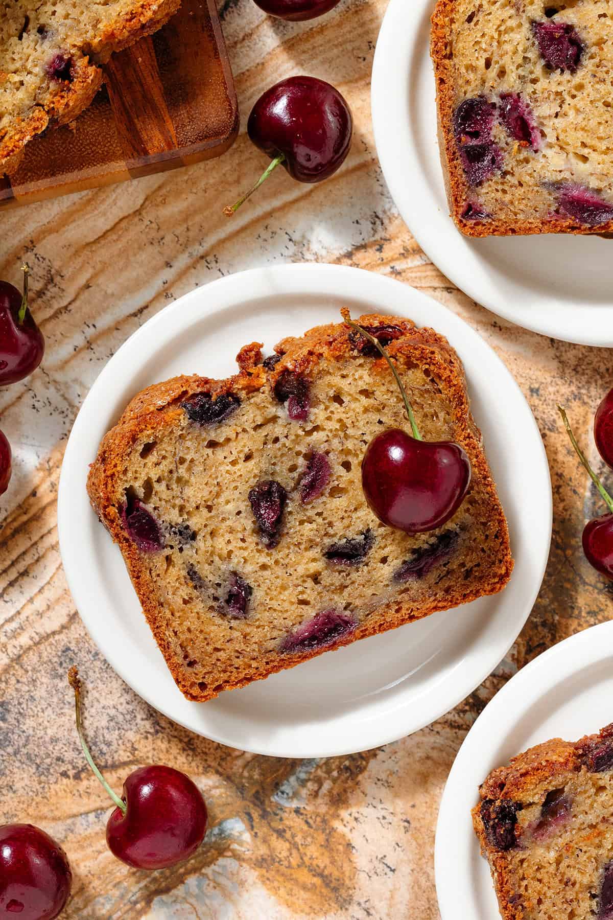 Slices of banana bread with cherries on small white plates.