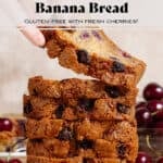 A stack of cherry banana bread slices on a small cutting board and a hand taking a slice off the top.