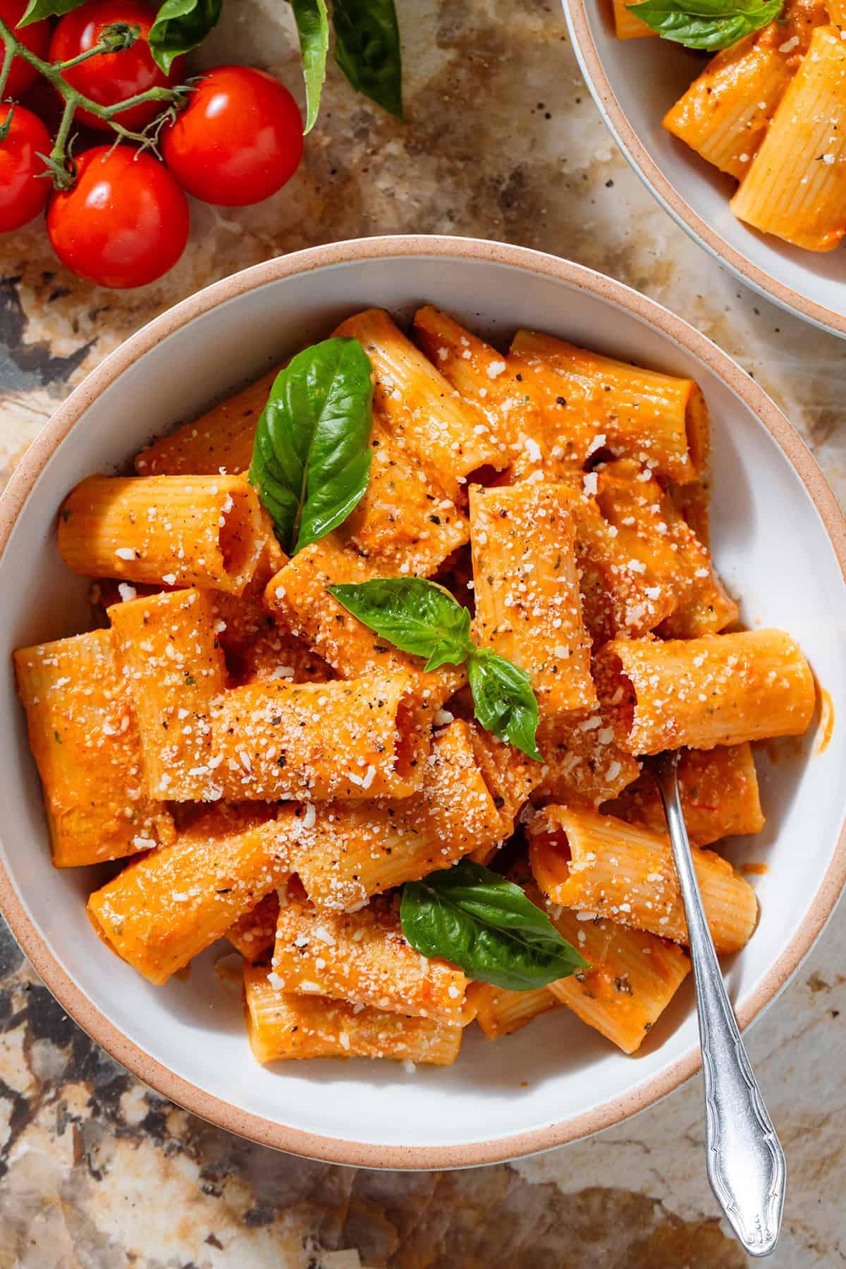 Creamy tomato pasta in a low white bowl topped with fresh basil and dusted with grated parmesan and black pepper with a fork inside the bowl on the right.