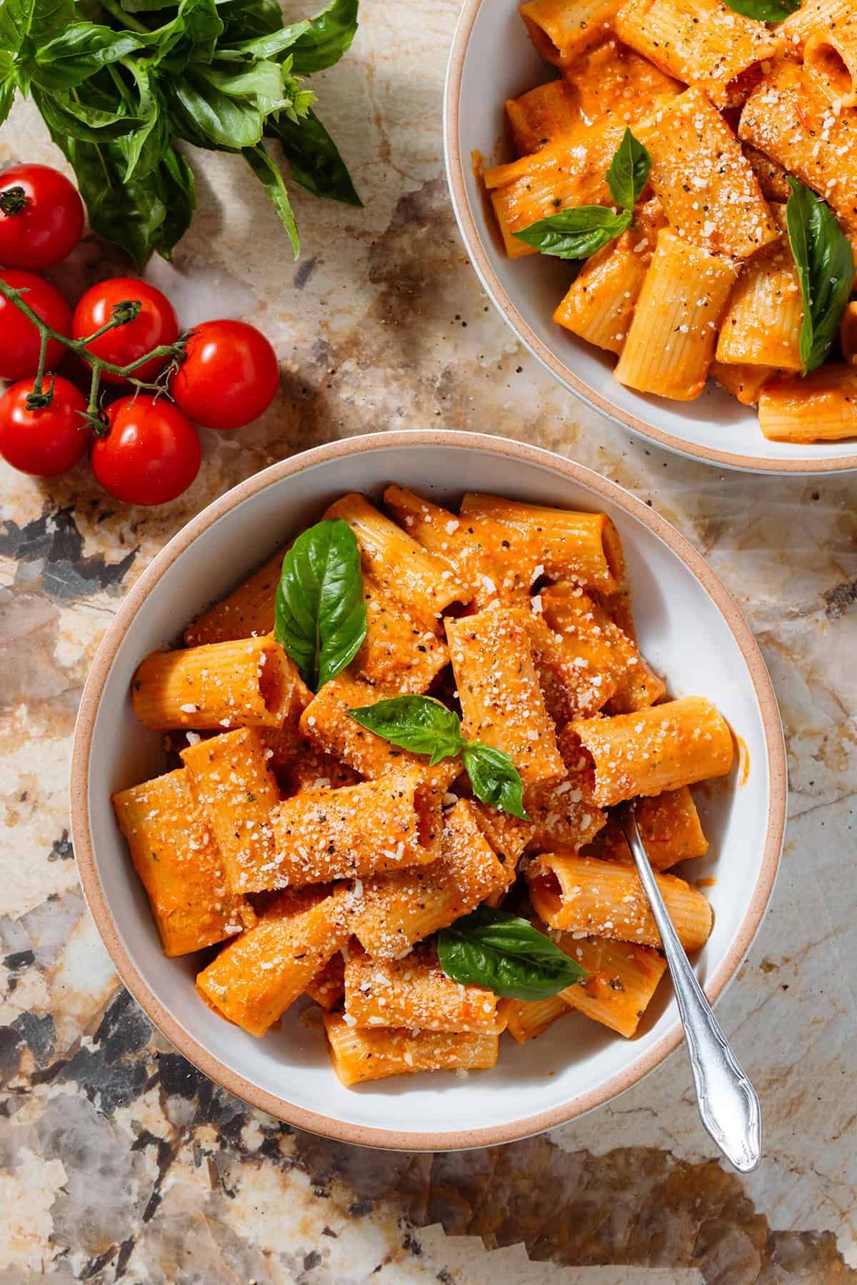 Creamy tomato pasta in a low white bowl topped with fresh basil and dusted with grated parmesan with a fork inside the bowl on the right.