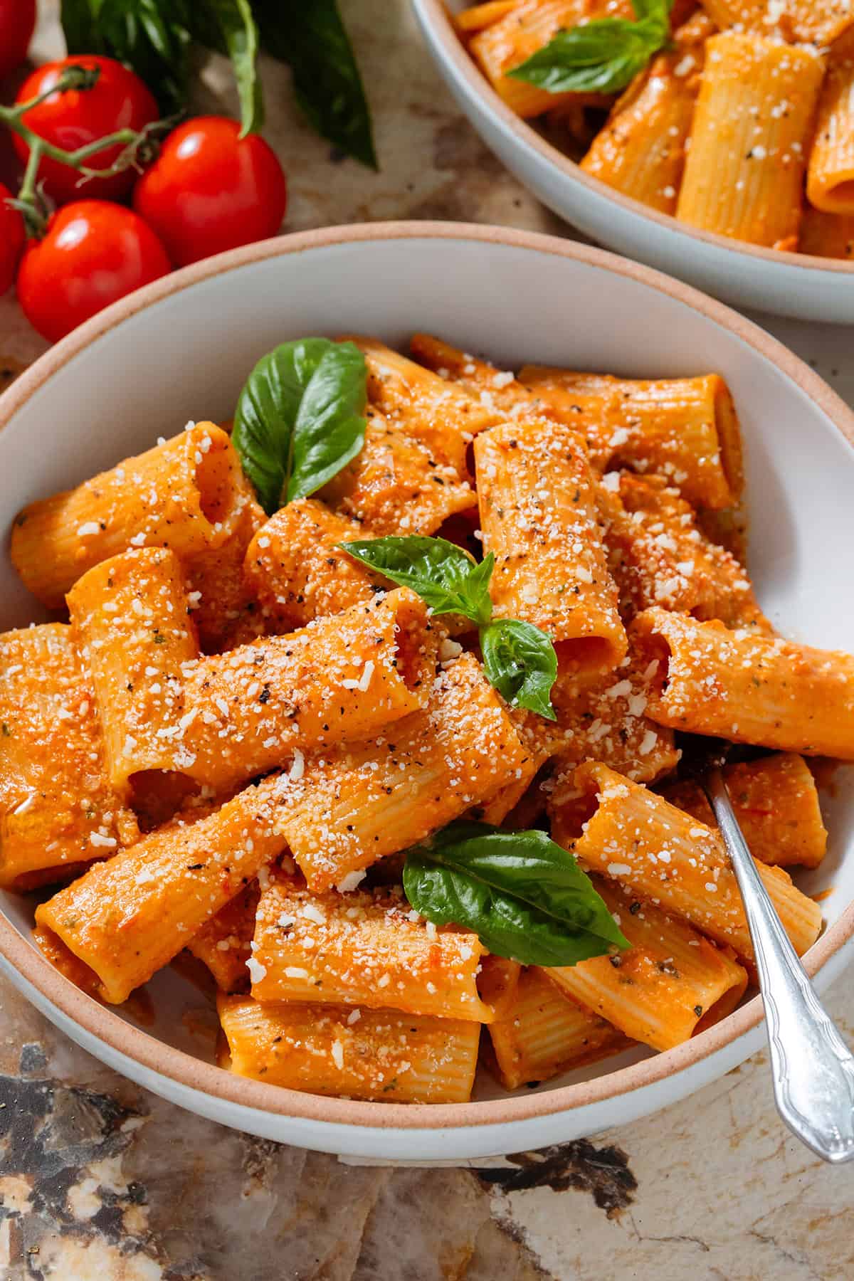 Creamy tomato pasta in a low white bowl topped with fresh basil and dusted with grated parmesan and black pepper with a fork inside the bowl on the right.