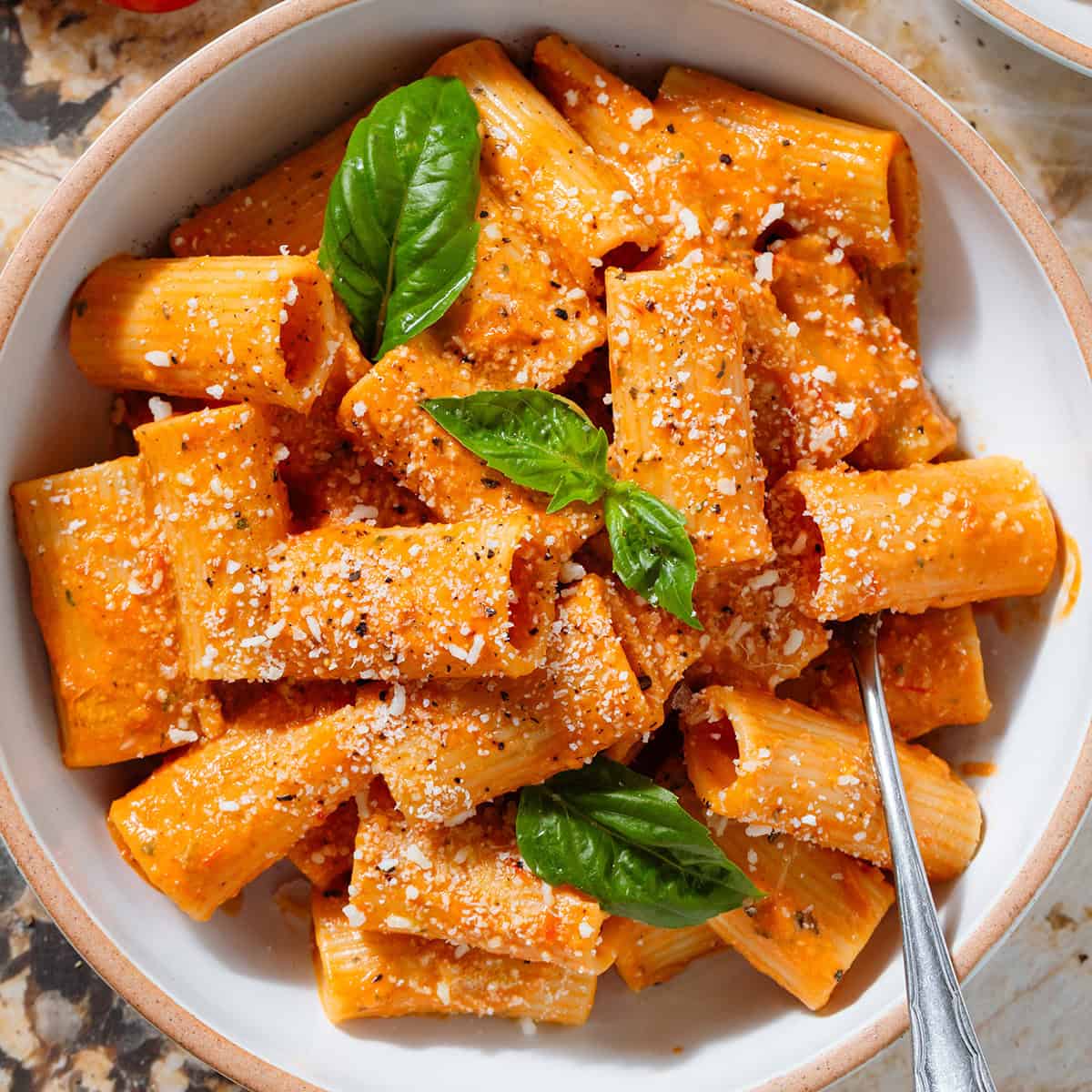 Creamy tomato pasta in a low white bowl topped with fresh basil and dusted with grated parmesan and black pepper.