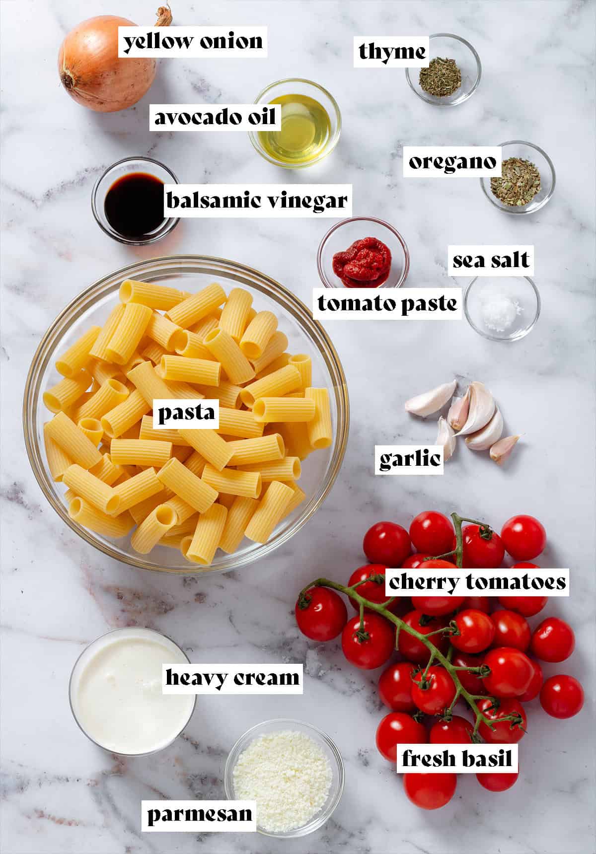 Dry pasta in a large bowl, cherry tomatoes, spices, avocado oil, tomato paste, and other ingredients in small glass bowls.