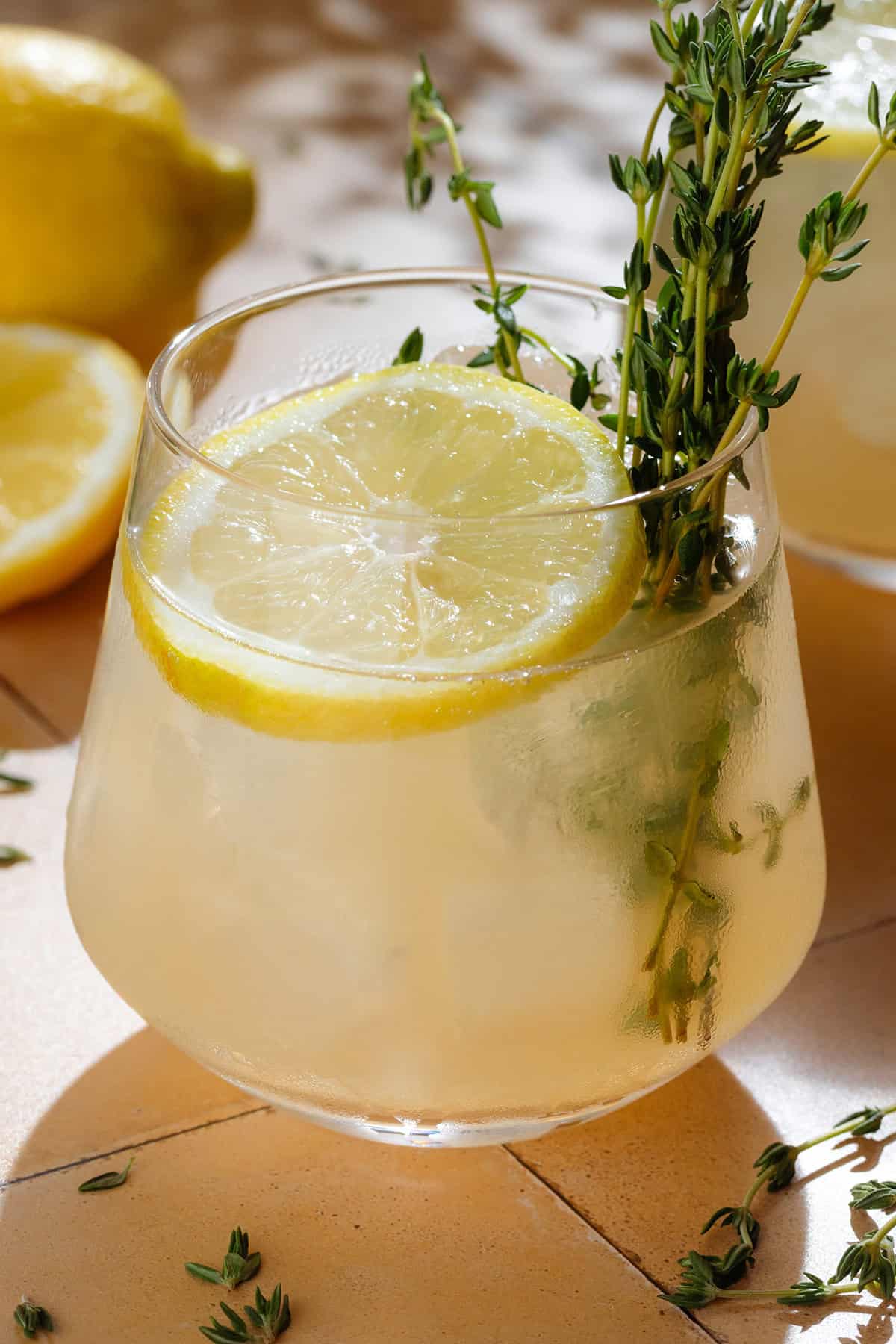 Light yellow thyme gin cocktail in a short glass with ice garnished with fresh thyme and a lemon slice.