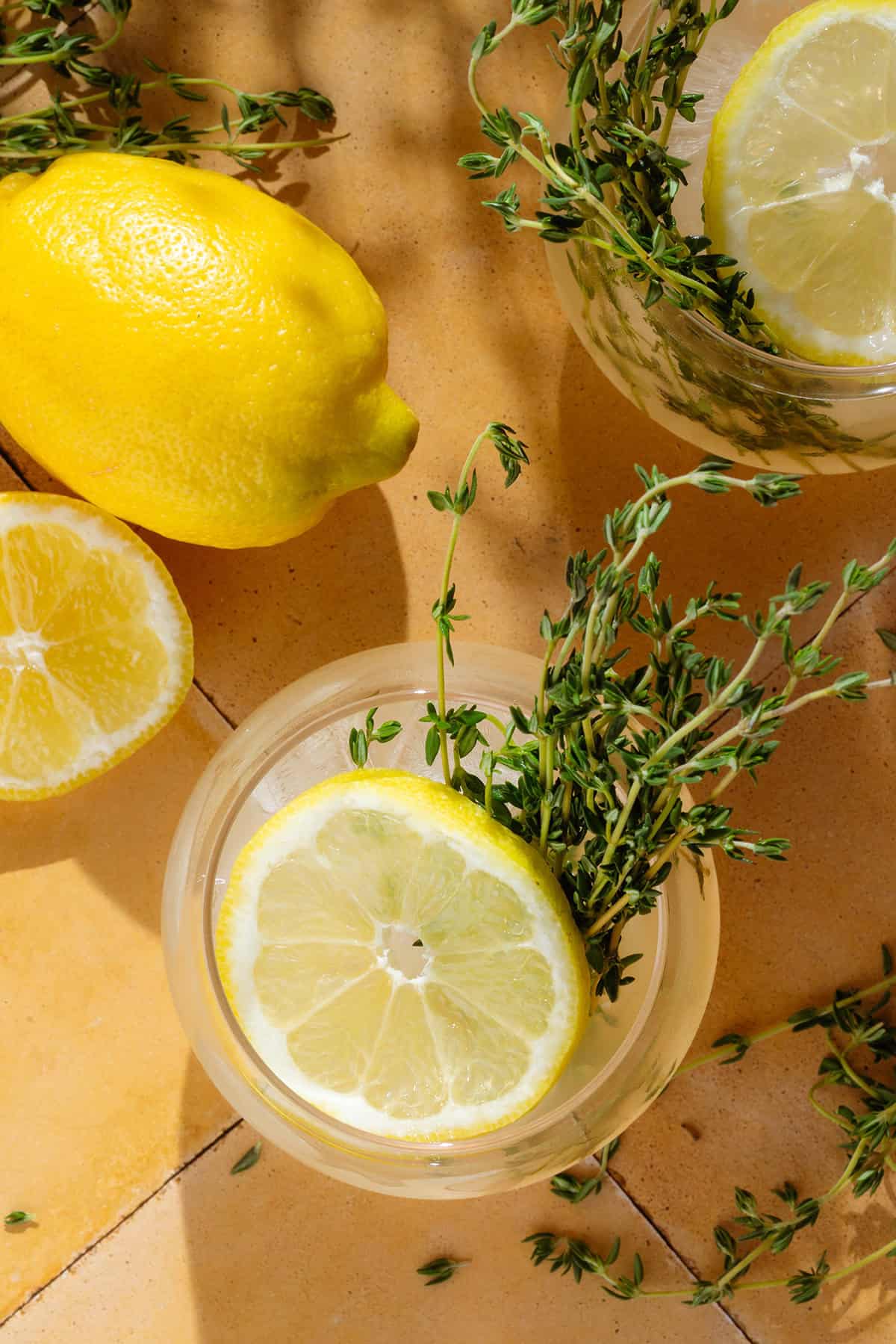 Two lemon thyme gin cocktails in short glasses garnished with a slice of lemon and fresh thyme.