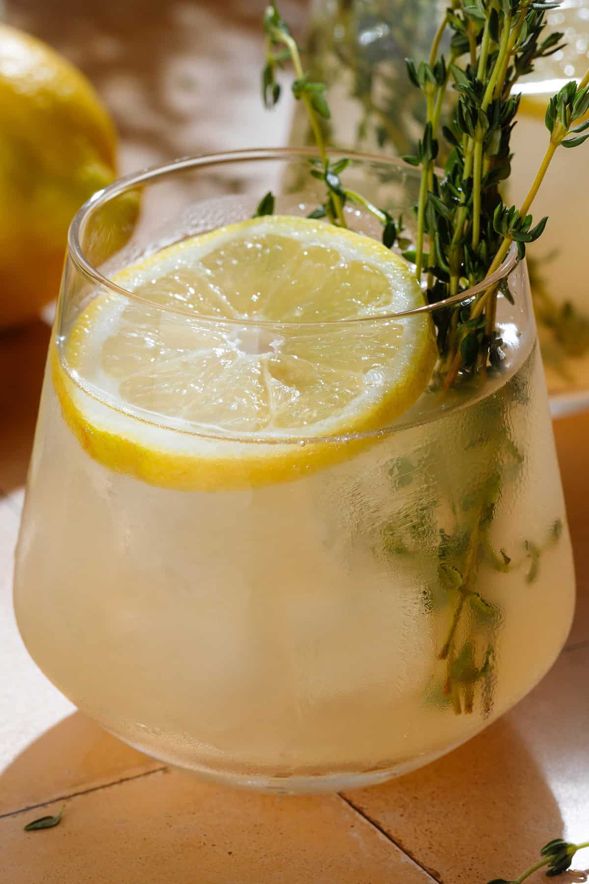 Light yellow thyme gin cocktail in a short glass with ice garnished with fresh thyme and a lemon slice.