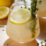 Light yellow thyme gin cocktail in a short glass with ice garnished with fresh thyme and a lemon slice.