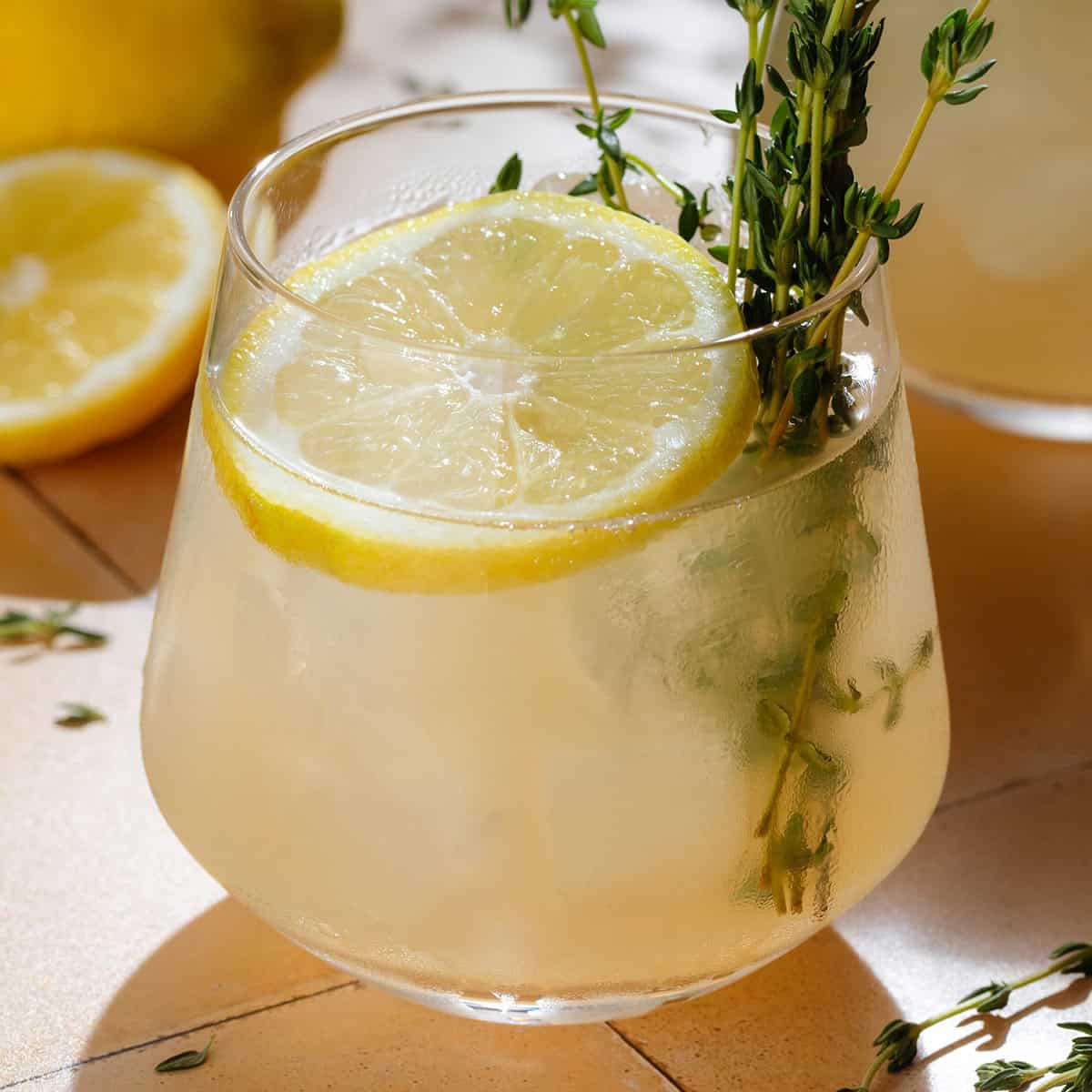 Light yellow thyme gin cocktail in a short glass with ice garnished with fresh thyme and a lemon slice.