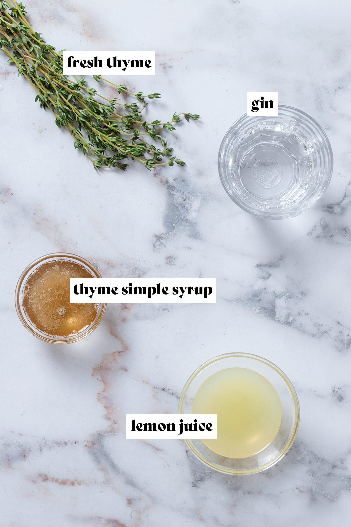 Gin, lemon juice, and thyme syrup in small glass bowls and fresh thyme on a marble background.