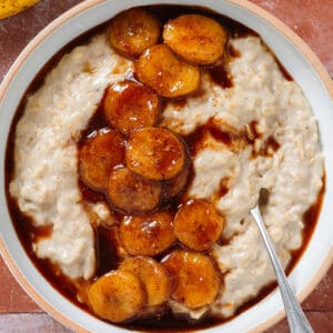 Creamy oatmeal in a white bowl topped with caramelized banana slices and sprinkled with cinnamon with a spoon in the bowl on the right.