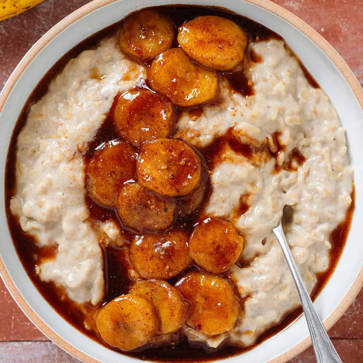 Creamy oatmeal in a white bowl topped with caramelized banana slices and sprinkled with cinnamon with a spoon in the bowl on the right.