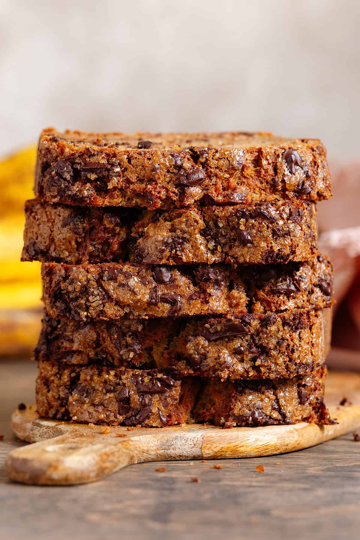 A stack of 5 chocolate chunk banana bread slices on a small wooden cutting board.