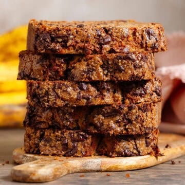 A stack of 5 chocolate chunk banana bread slices on a small wooden cutting board.