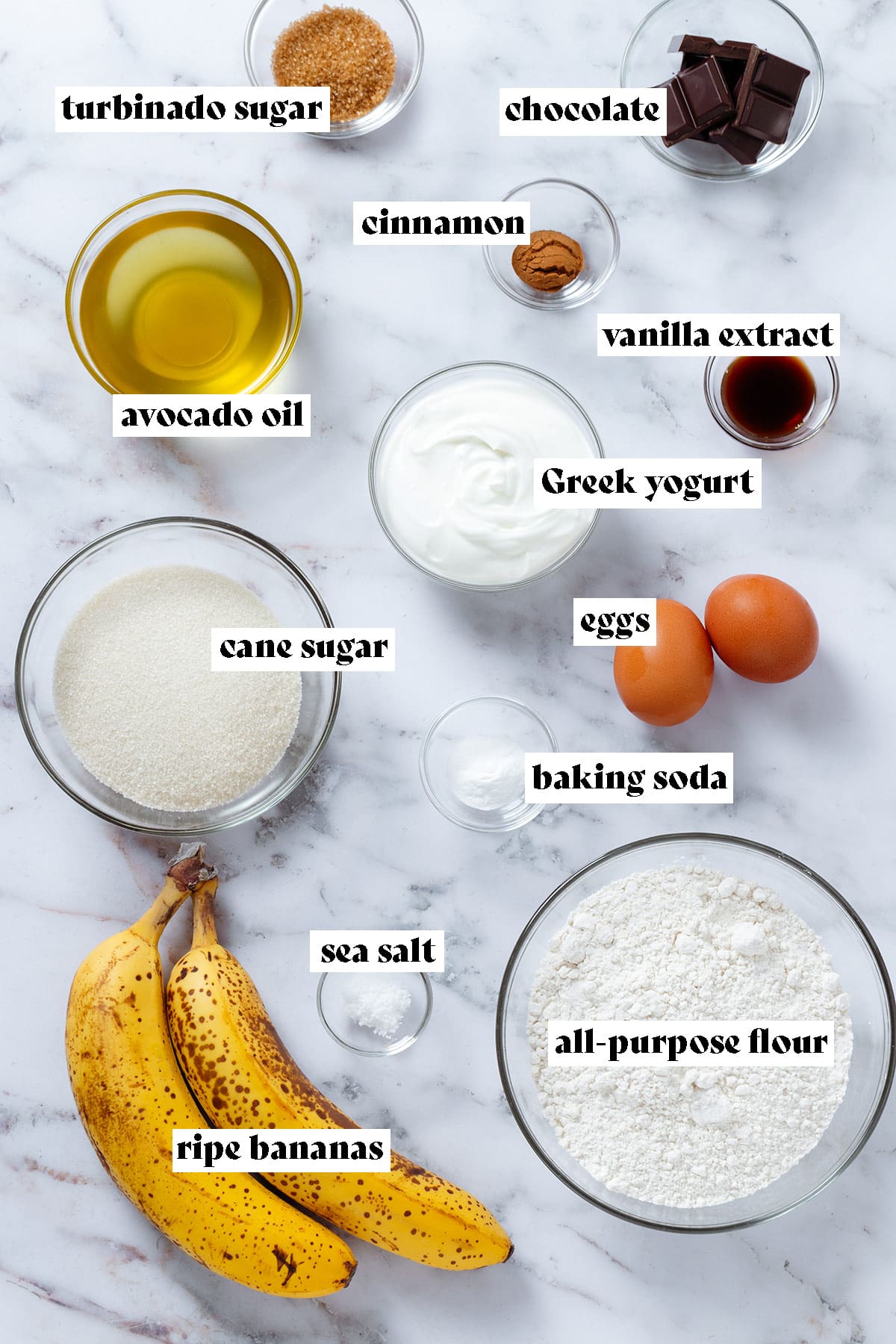 Ingredients like bananas, flour, sugar, Greek yogurt, avocado oil, vanilla extract, and spices in small glass bowls with text overlay.