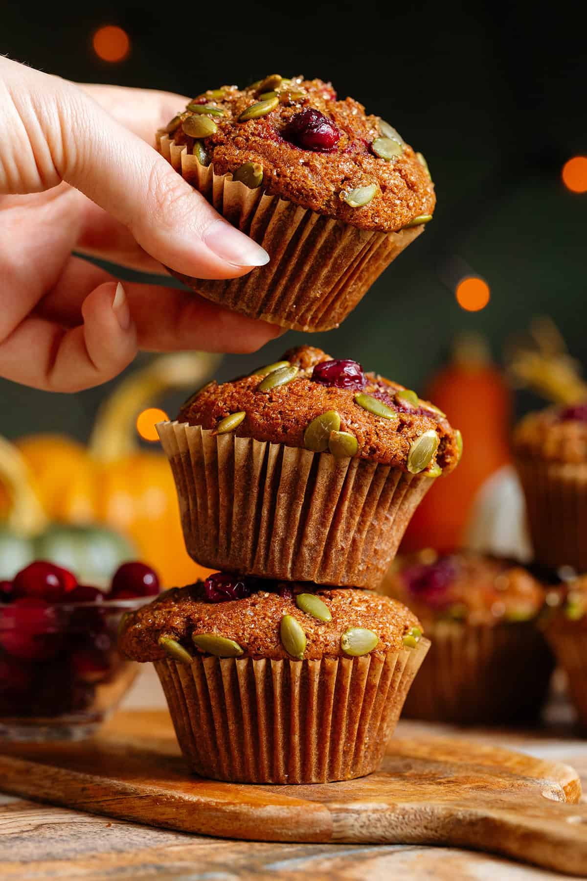 Two pumpkin muffins with cranberries and pumpkin seeds stacked on top of each other with a hand grabbing the one on top.