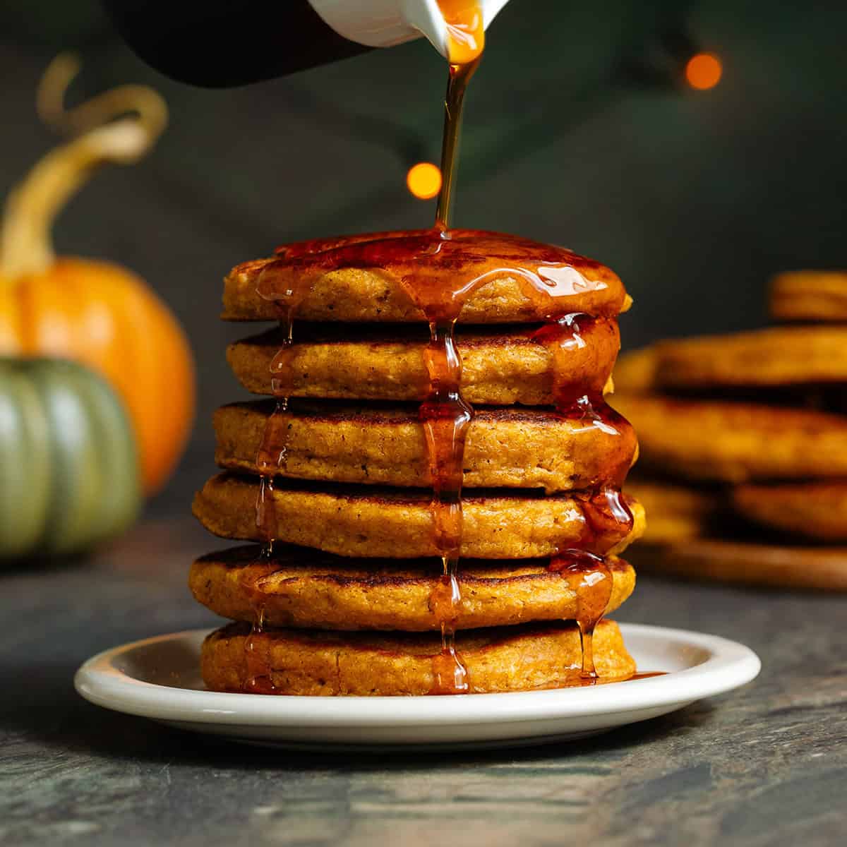 A stack of small pumpkin pancakes on a small beige plate on a green background.