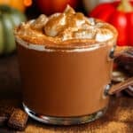 Creamy hot chocolate in a glass mug topped with whipped cream and dusted with pumpkin pie spice.