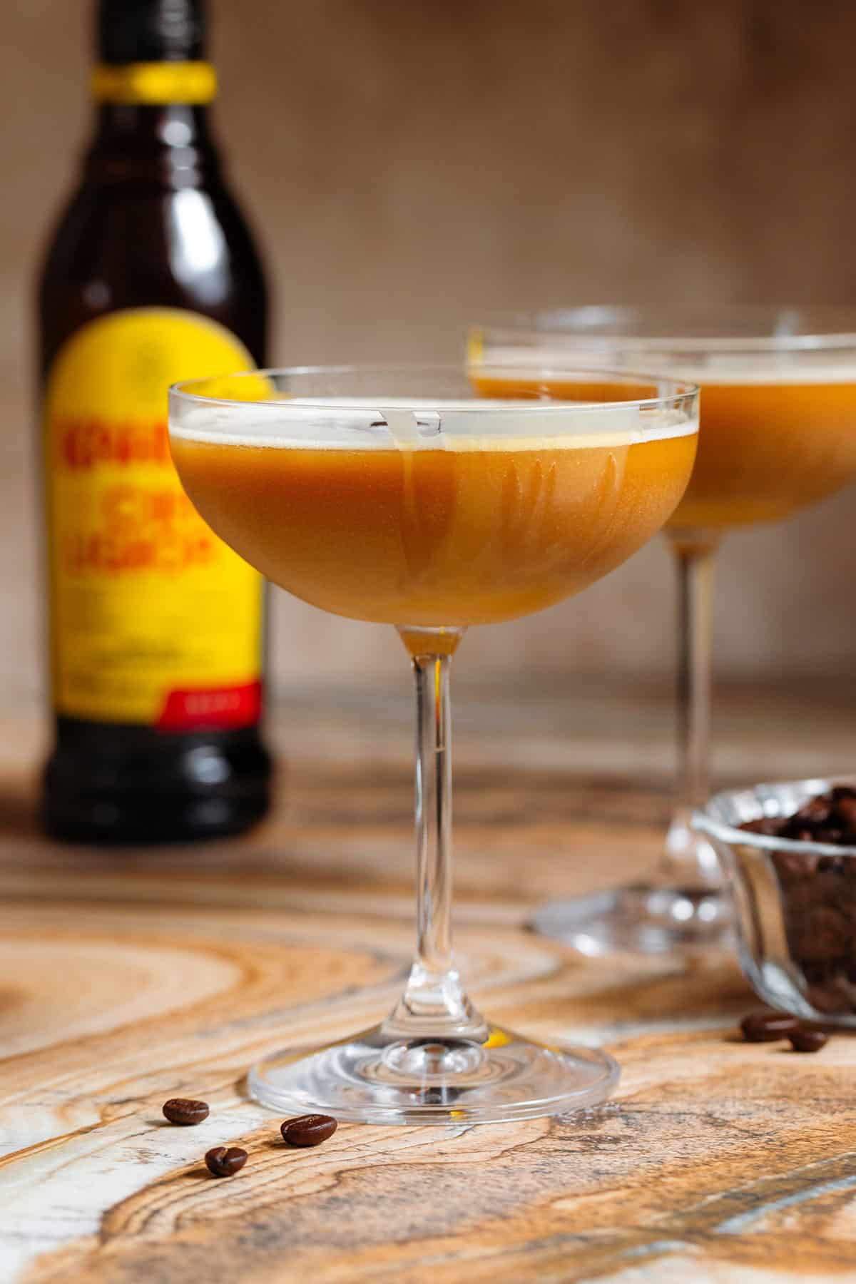 A coupe glass with caramel espresso martini with thin foam garnished with a drizzle of caramel sauce.