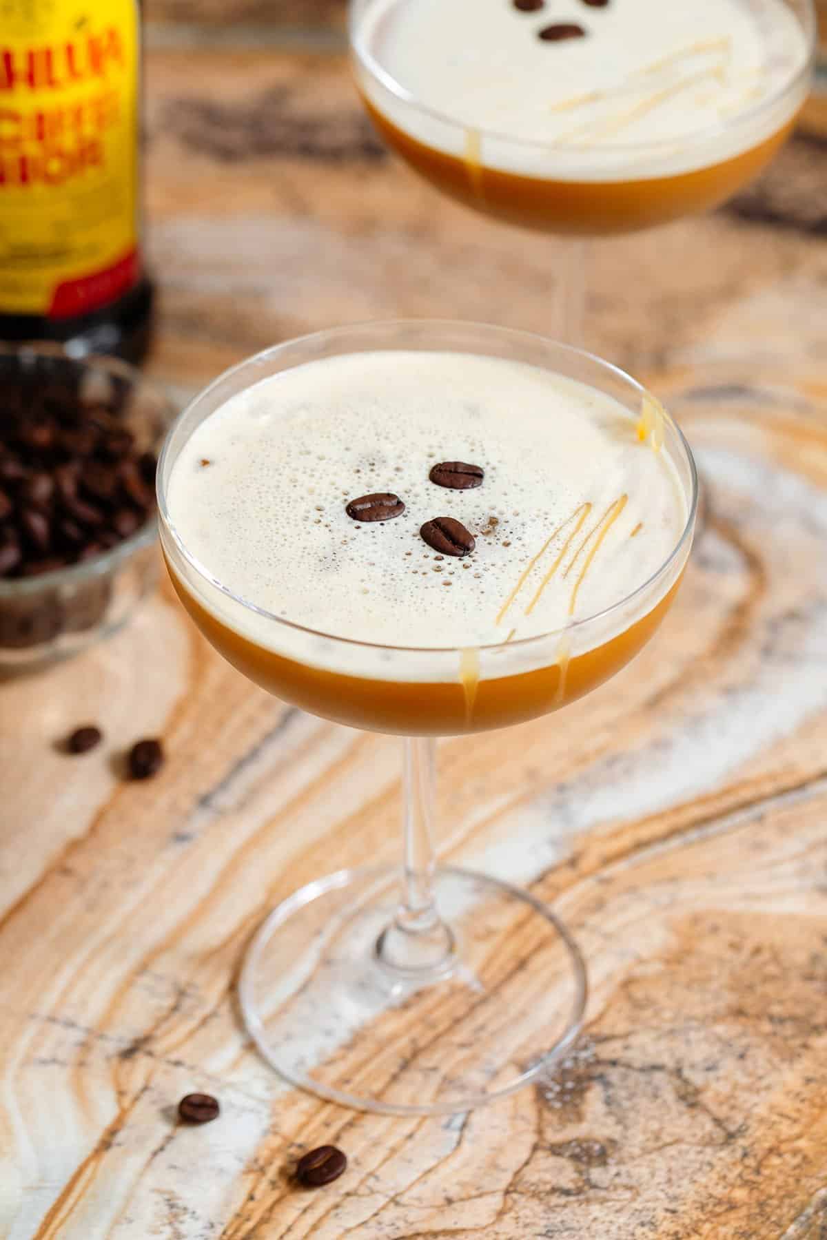 A coupe glass with caramel espresso martini garnished with 3 espresso beans and a drizzle of caramel sauce.
