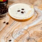 A coupe glass with caramel espresso martini garnished with 3 espresso beans and a drizzle of caramel sauce.