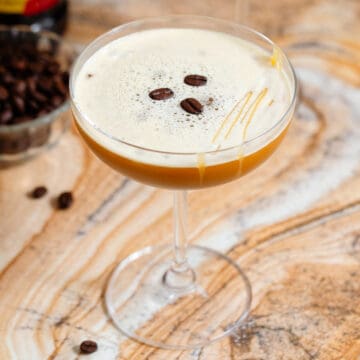 A coupe glass with caramel espresso martini garnished with 3 espresso beans and a drizzle of caramel sauce.