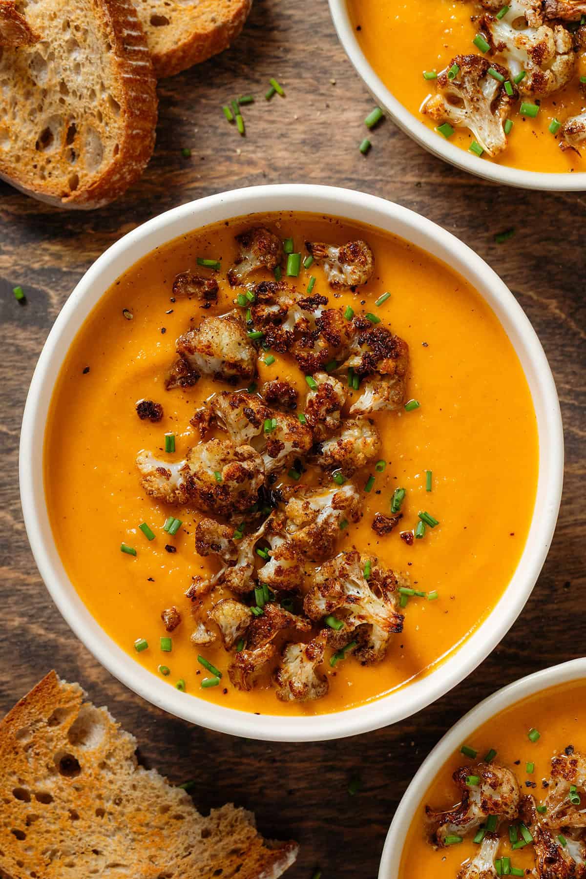 A white bowl with creamy sweet potato and cauliflower soup with caramelized cauliflower florets and chopped chives on top.